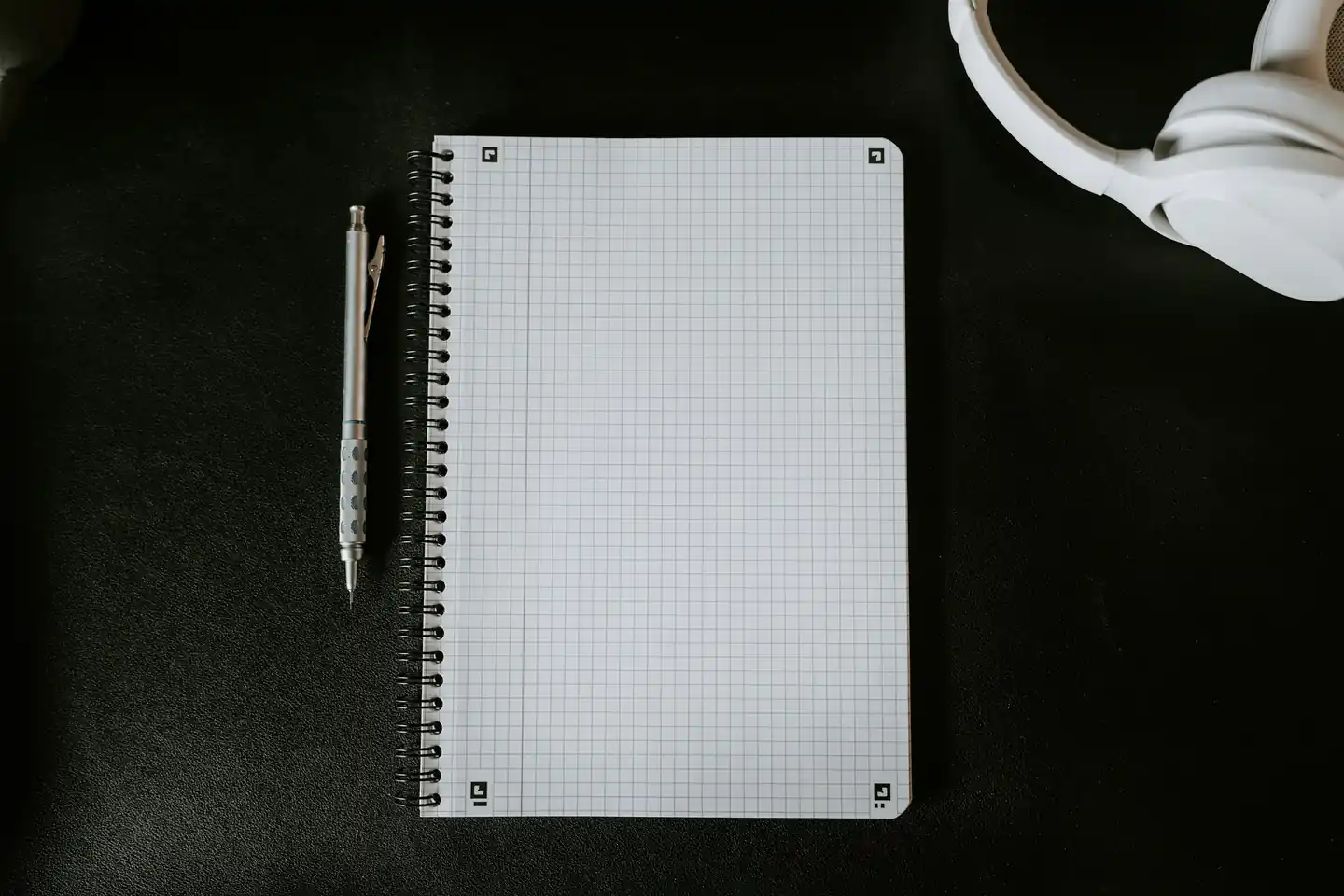 An open grid notebook and a pen on a dark desk, ready to work a month of spending into a plan