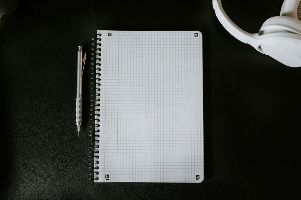 An open grid notebook and a pen on a dark desk