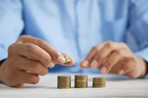 A hand adding one more coin to three small stacks on a table